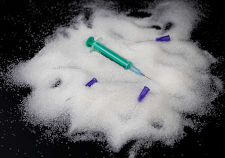 Medical needles, syringe and sugar on a black background. The concept of the harmful effects of...