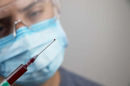 A male doctor looks at a syringe with blood. Blood sampling for analysis in the laboratory. Light background and place for text.の写真素材
