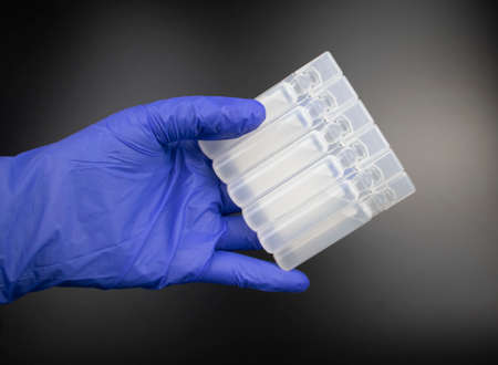 Plastic ampoules with medicine or vaccine close-up. The doctor in blue gloves examines the medicine....
