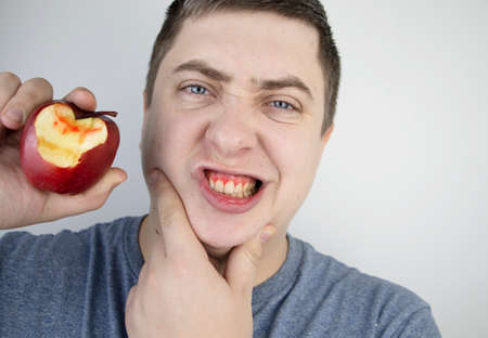 A man bit an apple and blood came out of his gums. Gum bleeding, symptoms of gingivitis, periodontitis and periodontal disease.の写真素材
