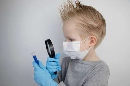 The child plays a doctor and a scientist. A boy in a medical mask studies a medicine in a test tube through a magnifying glass. The concept of education and promotion of medical professionsの写真素材