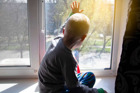 Pandemic isolation - outbreaks of coronovirus, covid-19. The child sadly looks out the window,...