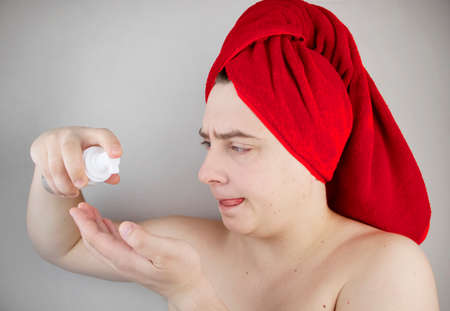 Funny man with a red towel on his head takes care of his face and uses a foam for washing. The concept of male self-care, spa treatments and male cosmeticsの写真素材