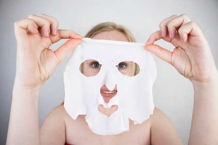 A cheerful and funny girl fooling around and grimacing in a moisturizing face mask. Morning beauty treatments, oily and combination skin care concept.の写真素材