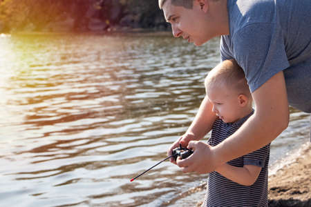 Dad and son launch a ship on the radio. Father shows the boy how to play with the boat on the remote control. The concept of relaxing on the beach and a happy childhoodの写真素材
