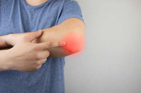 A man suffers from elbow pain. Damaged elbow joint, bone fracture, or sprain. Hand injury and flexion pain conceptの写真素材