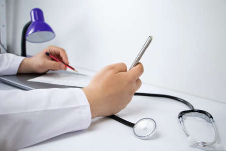 The doctor is holding a smartphone. Medical consultation by phone. Mobile app for healthcare providersの写真素材