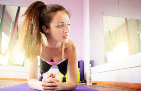 A thin and fit girl is engaged in sports and yoga on the rug alone. Bright room with wooden floors...