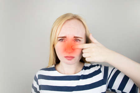 A young woman touches her nose, which is very painful. Medical care concept for difficulty...