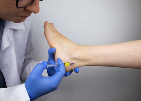 An orthopedic surgeon injects medicine into the Achilles tendon to relieve pain. Help treat sprains, trauma or injury.の写真素材