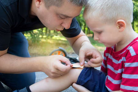 A four-year-old boy fell off a scooter and broke his knee. Dad provides first aid by disinfecting...