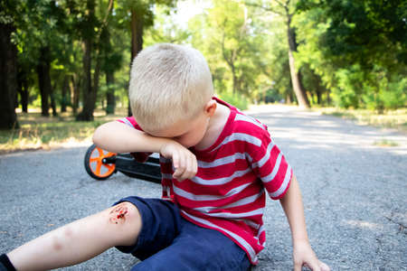 A four-year-old boy fell off a scooter and broke his knee. Dad provides first aid by disinfecting the wound and applying a plaster.の写真素材