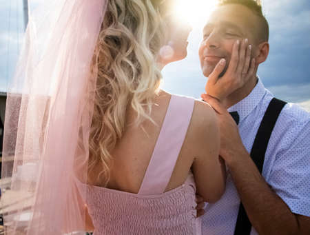 Creative hipster wedding by the sea. The bride is in a pink dress and veil, the groom is in beautiful trousers with suspenders and a youth shirt. Madness, fun and an unusual approach to marriageの写真素材