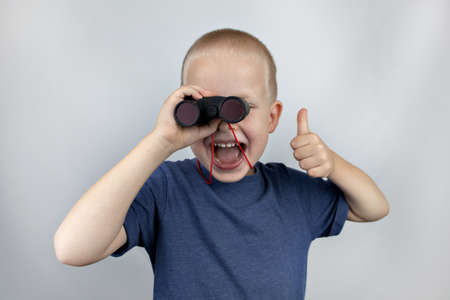 A boy with binoculars looks into the distance and smiles. Facial expression and body position show...
