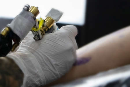 A tattoo artist fills a drawing on a man's hand with a typewriter. The concept of overcoming pain, courage, creativity and thinking outside the boxの写真素材