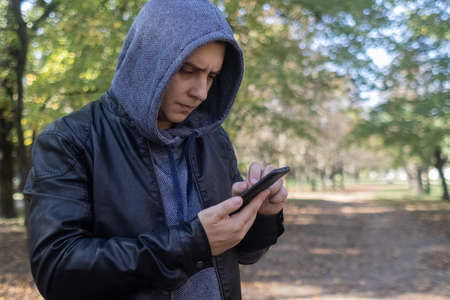 A man in a leather jacket looks at the phone in the middle of the forest. Social media immersion, orienteering, and phone stress conceptの写真素材