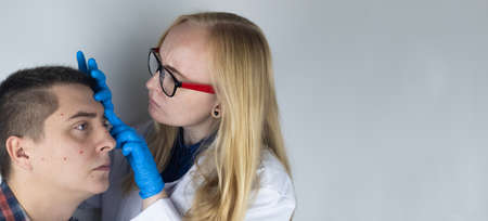 An allergist or dermatologist examines red spots on a man's face.