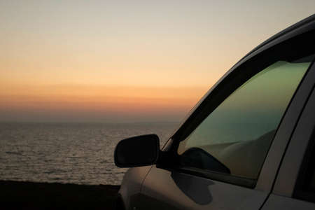 The car is standing over a cliff by the sea. The sunset rays of the sun are reflected in the glass....