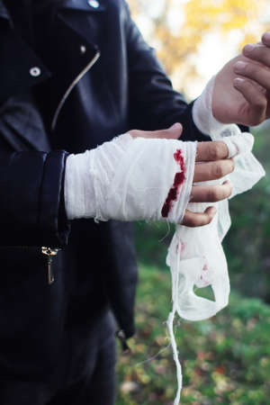 Man with bandage with blood on the knuckles, natural background. End of fight, fight, blood and aggression concept. A man in a leather jacket.の写真素材