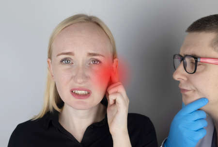 A woman suffers from pain in the ear. The auditory meatus hurts due to otitis media, cerumen plug, ear boil, or trigeminal neuralgia. On examination by a doctor.の写真素材