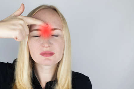 Nasal bridge pain, headache. A woman holds his nose with his hand and winces in pain. Signs of acute ethmoiditis. On examination by a doctor.の写真素材