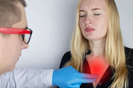 A woman grabs his chest in the region of the heart. Heart attack or chest pain. The concept of heart disease and its pain manifestations. On examination by a doctor.の写真素材
