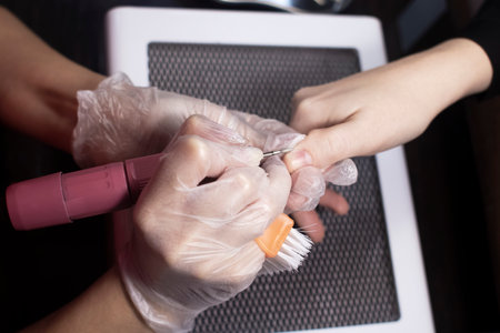 The manicurist processes the woman's nails with an electric file. Professional care in a beauty salon. Manicure process. Close-up of a specialist's workの写真素材