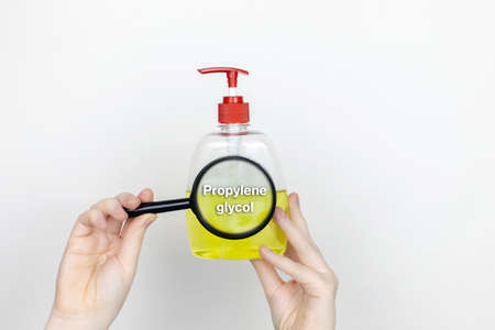 A woman examines the harmful ingredients of the liquid soap a magnifying glass. Harmful composition...