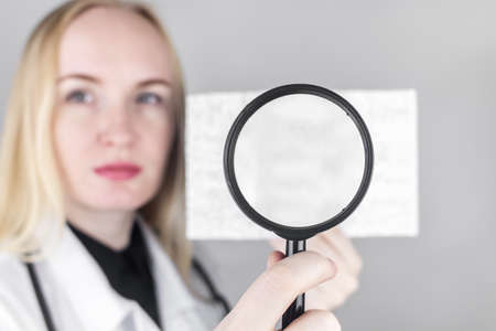 A neurologist with a magnifying glass examines an encephalogram of a patient's brain. Schedule of electroencephalograms - study of brain currents for signs of epilepsy and pathologiesの写真素材