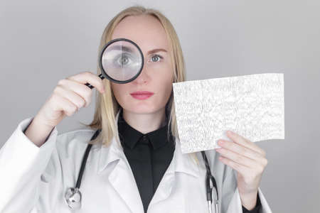 A neurologist with a magnifying glass examines an encephalogram of a patient's brain. Schedule of electroencephalograms - study of brain currents for signs of epilepsy and pathologiesの写真素材
