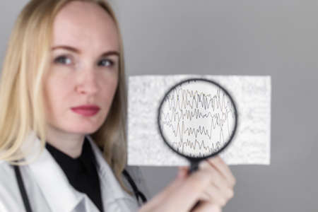 A neurologist with a magnifying glass examines an encephalogram of a patient's brain. Schedule of electroencephalograms study of brain currents for signs of epilepsy and pathologiesの写真素材