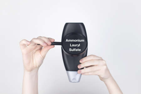 Chemical components on the shampoo label: Ammonium Lauryl Sulfate. Female hands hold a magnifying...