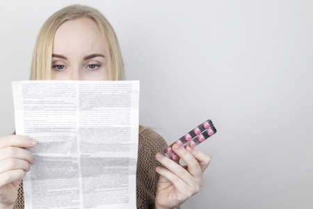 The girl on a white background reads the instructions for medicines. The woman looks at the list and...