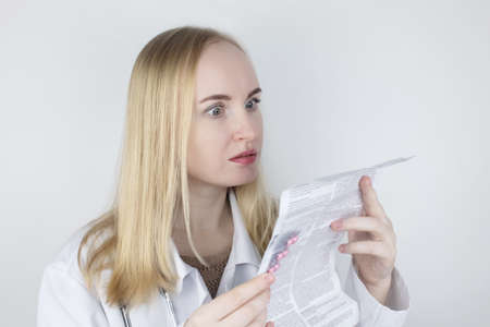 The doctor on a white background reads the instructions for medicines. The specialist looks at the list and composition of the drug. The concept of a professional treatment appointmentの写真素材