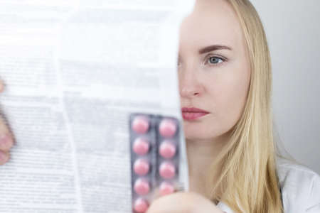 The doctor on a white background reads the instructions for medicines. The specialist looks at the list and composition of the drug. The concept of a professional treatment appointmentの写真素材