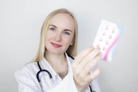 A specialist in a white coat holds pills in his hand. Recommendations of the attending physician about taking the pills. Pharmacist advertises drugs. Correct medication prescription.の写真素材