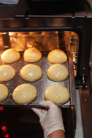 Baker puts their buns in the oven, which he had previously greased with butter and sprinkled with...
