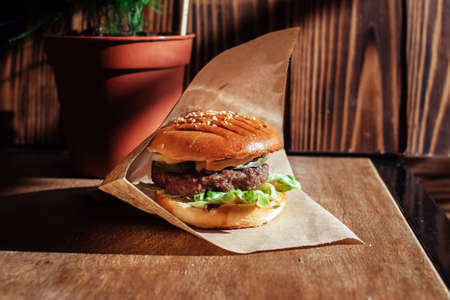 Burger in paper packaging close-up. Food in a fast food restaurant. Macro photo of burger ingredients with meat and vegetablesの写真素材