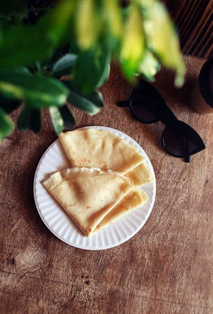 Pancakes drizzled with red syrup on a plate in a restaurant. Breakfast at the cafe. A woman eats pancakes for breakfast from disposable dishes. Top view and vertical photoの写真素材