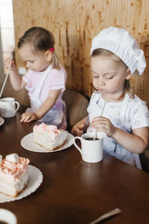Children in the kitchen cook with their parents. Making homemade cake, pastries or cookies for the whole family. Happy childhood concept. Little twin sisters in kitchen aprons and chef hatsの写真素材