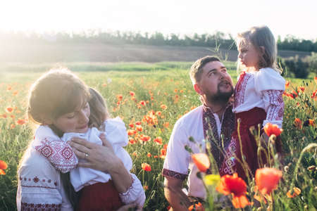 A family in a poppy field dressed in a national Slavic costume. Mom, dad and twin girls in embroidered shirts frolic on sunny day. Concept of a happy childhood, history and togetherness with ancestorsの写真素材