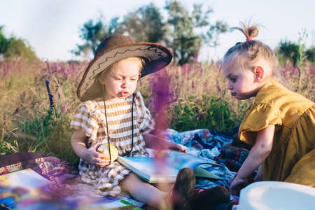 Little sisters in the field at a picnic. Girls sit on a bedspread among sage and lavender. There are...