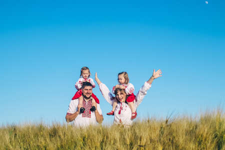 A family in a poppy field dressed in a national Slavic costume. Mom, dad and twin girls in embroidered shirts frolic on sunny day. Concept of a happy childhood, history and togetherness with ancestorsの写真素材