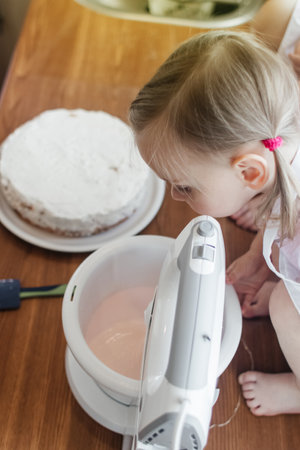 Children in the kitchen cook with their parents. Making homemade cake, pastries or cookies for the whole family. Happy childhood concept. Little twin sisters in kitchen aprons and chef hatsの写真素材