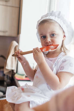 Children in the kitchen cook with their parents. Making homemade cake, pastries or cookies for the whole family. Happy childhood concept. Little twin sisters in kitchen aprons and chef hatsの写真素材