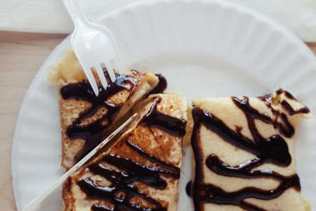 Pancakes drizzled with chocolate on a plate in a restaurant. Breakfast at the cafe. A woman eats...