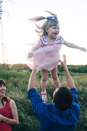 Dad and daughter play together on the flower field. Happy and caring father is having fun with his daughter. Dad pays attention to his child. Bearded man and little girl with flowers in their hairの写真素材