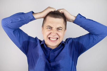 A male businessman in a blue shirt shouts loudly at his subordinates. Breakdown and hysteria. Close-up of an angry face. Saliva flows from the mouth and sweat stains are visible on clothes and faceの写真素材