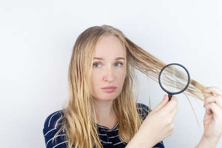 The girl looks in front of the magnifier at her oily hair. Problematic scalp and increased secretion of the sebaceous glands. Hair care. Oily hair care and treatment conceptの写真素材