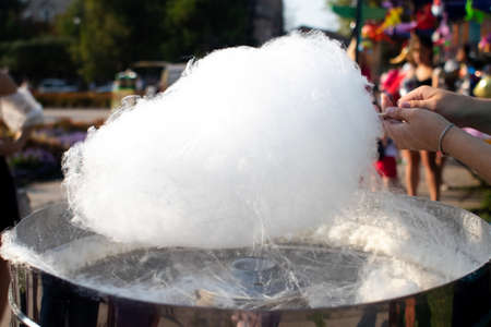 Close-up of the hands of a man who makes cotton candy. Wooden stick will wind the threads of the...